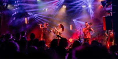 Aufnahme aus dem Publikum: Bühne in blauem und rotem Licht. Drei Blasinstrumente, ein Kontrabass und ein Schlagzeug werden gespielt.