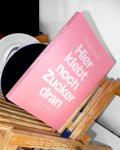 Ein aufgeschlagenes Buch, auf der linken Seite steht ein kurzer Text, auf der rechten Seite ist die Fotografie einer Rahmtorte mit Himbeergarnitur zu sehen.