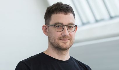 Ein Mann mit Brille und Bart, in schwarzem T-Shirt, blickt gerade in die Kamera.