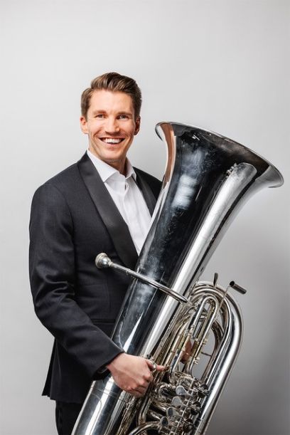 Ein Mann hält eine Tuba in der Hand und lacht in die Kamera.