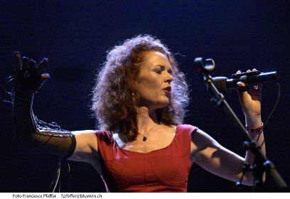 Eine Frau steht auf der Bühne. Sie hat ein Mikrofon in der Hand und singt.