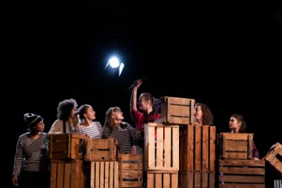 Sieben Frauen stehen hinter Holzkisten auf der Bühne.