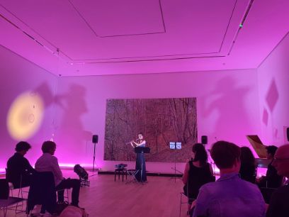 Konzertsaal, ein Bild an der Wand, Studentin Yvonne Gisler spielt ein Instrument, Raum ist in verträumte pink-rosa Farben getaucht.