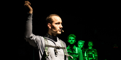 Bühnensituation, Schauspieler*innen hintereinander aufgereiht in grünem Licht