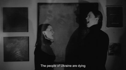 Standbild aus einem Video in Schwarzweiss, in dem sich eine Sängerin, links, und ein Sänger, rechts, vor einer Wand mit Bildern gegenüber stehen. Darunter steht der Untertitel: The people auf Ukraine are dying.