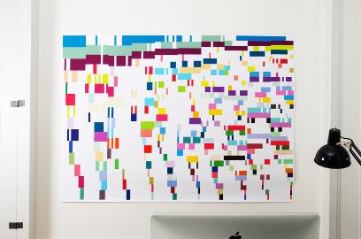 An einer weissen Wand ist ein weisses Plakat in Querformat mit verschiedenen farbigen Strichen auf mehreren Zeilen zu sehen.