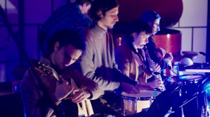 Eine Musikgruppe auf der Bühne, von der Seite aufgenommen.