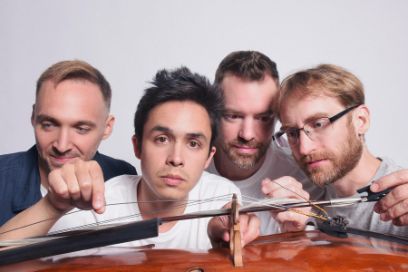 Bust portrait of four young men behind a lying cello.