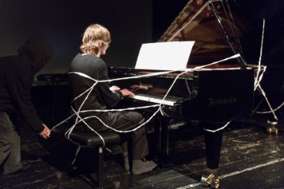 Person an Piano wird mit weissem Band eingewickelt