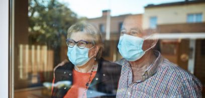 Besorgtes älteres Ehepaar mit Gesichtsmasken am Fenster