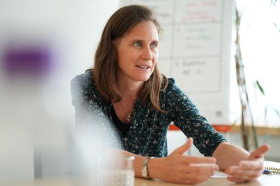 Jasmin Bischof sitzt gestikulierend an einem Tisch vor einem Flipchart.