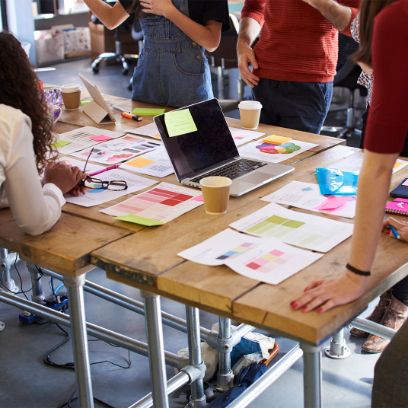 Studierende stehen um einen Tisch mit Post-its und Laptops