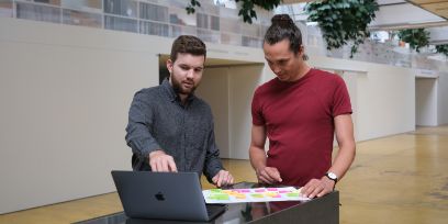 Zwei junge Männer diskutieren ein Projekt an einem Laptop.
