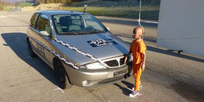Ein Kinder-Crash-Test-Dummy steht vor einem Crash-Test-Auto