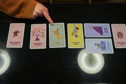 Hand zeigt mit Zeigefinger auf eine bunte Piktogrammkarte in einer Reihe verschiedener Karten-