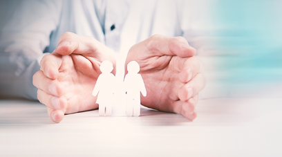 Zwei Hände, die sich beschützend um zwei Papierfiguren schmiegen
