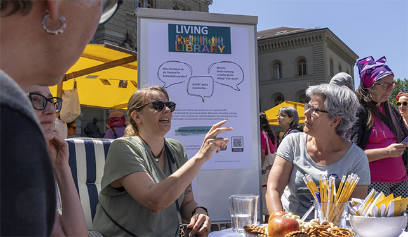 Menschen an einem runden Tisch und dahinter ein Flipchart mit Visualisierungen.