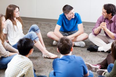 Schüler_innen und Lehrer sitzen im Kreis