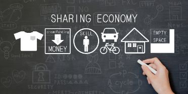 Eine Hand zeichnet mit Kreide Piktogramme an eine Wandtafel, um das Konzept der Sharing Economy zu erklären.