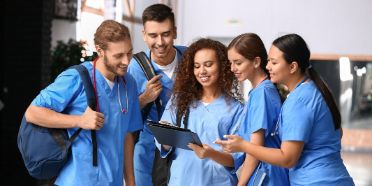 Fünf junge Pflegefachpersonen schauen auf ein Tablet.