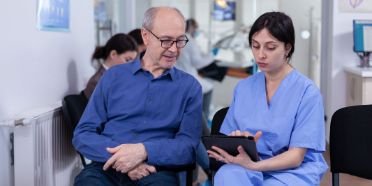 Pflegefachfrau mit Tablet spricht mit Patient im Warteraum